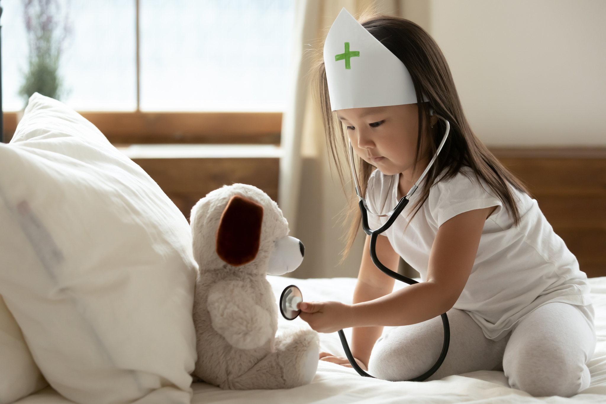 Asian little girl hold phonendoscope listens heartbeat to stuffed toy